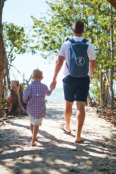 brett ekblom walking to the beach with a vineyard vines backpack, holding his son's hand